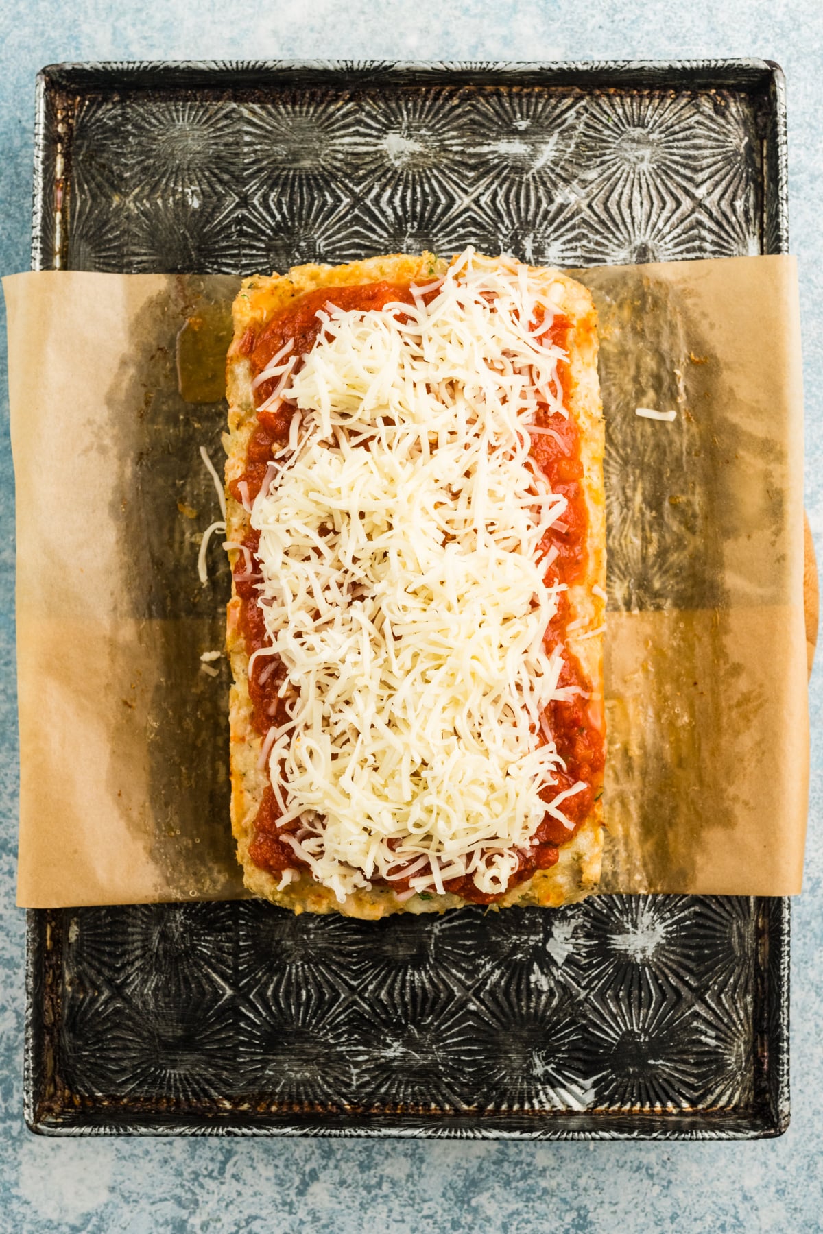 Partly baked parmesan chicken meatloaf removed from the pan and topped with marinara sauce and shredded cheese.