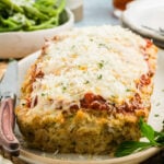 Parmesan chicken meatloaf topped with marinara and melted cheese on a platter next to a knife.