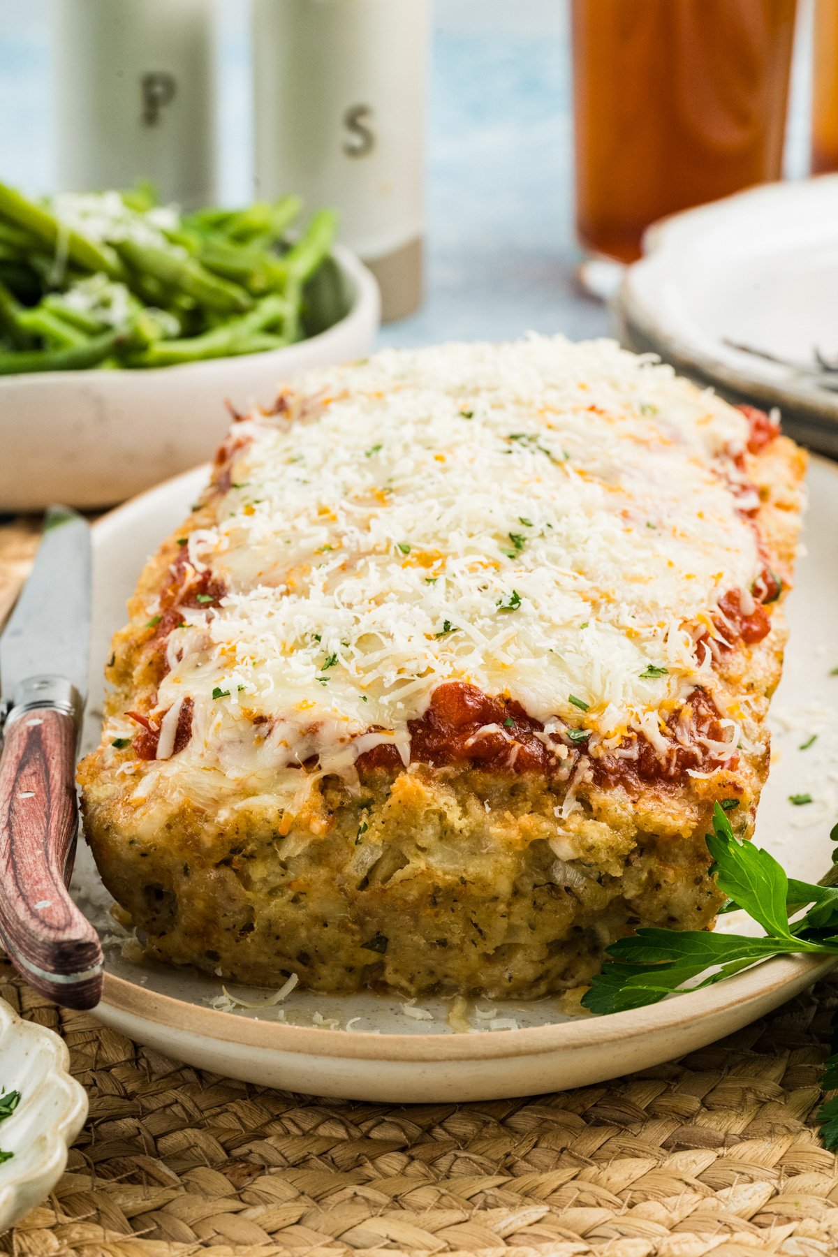 Parmesan chicken meatloaf topped with marinara and melted cheese on a platter next to a knife.