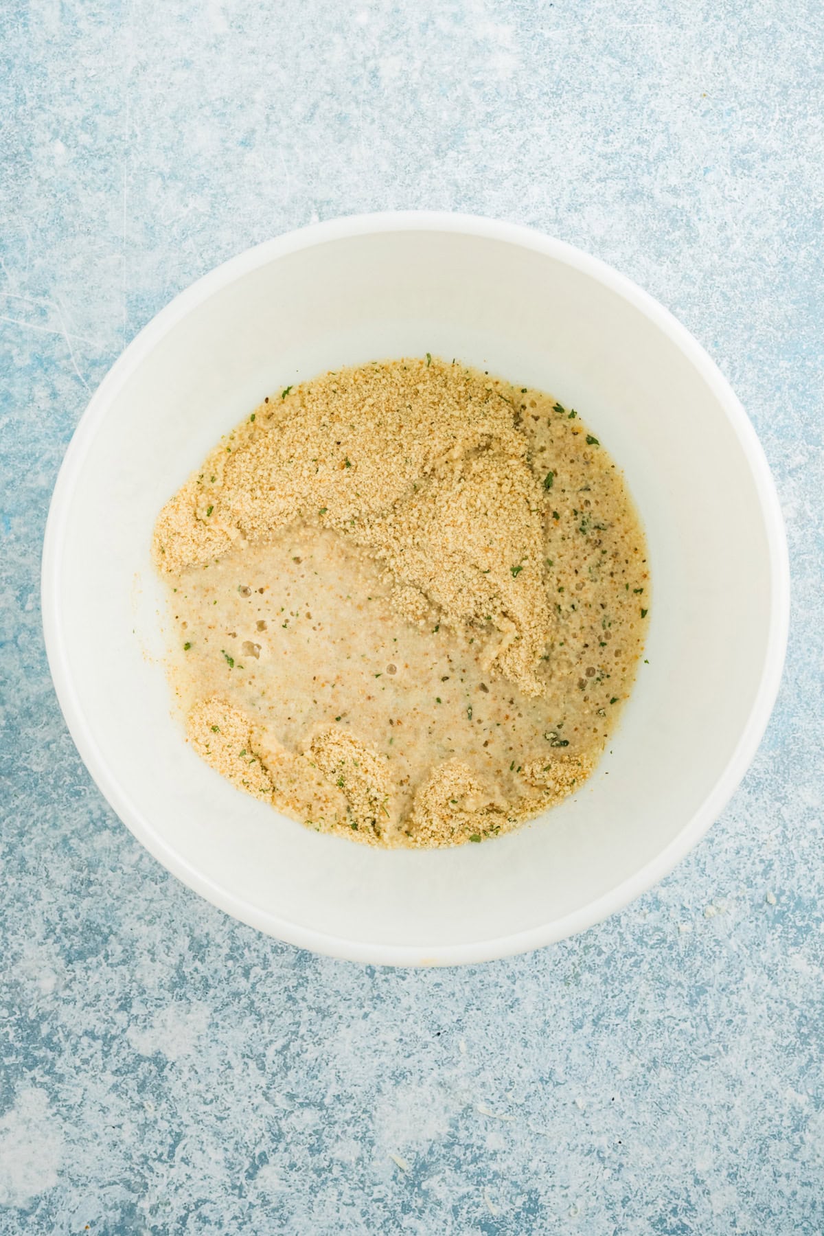 Italian breadcrumbs soaking in milk in a white bowl.