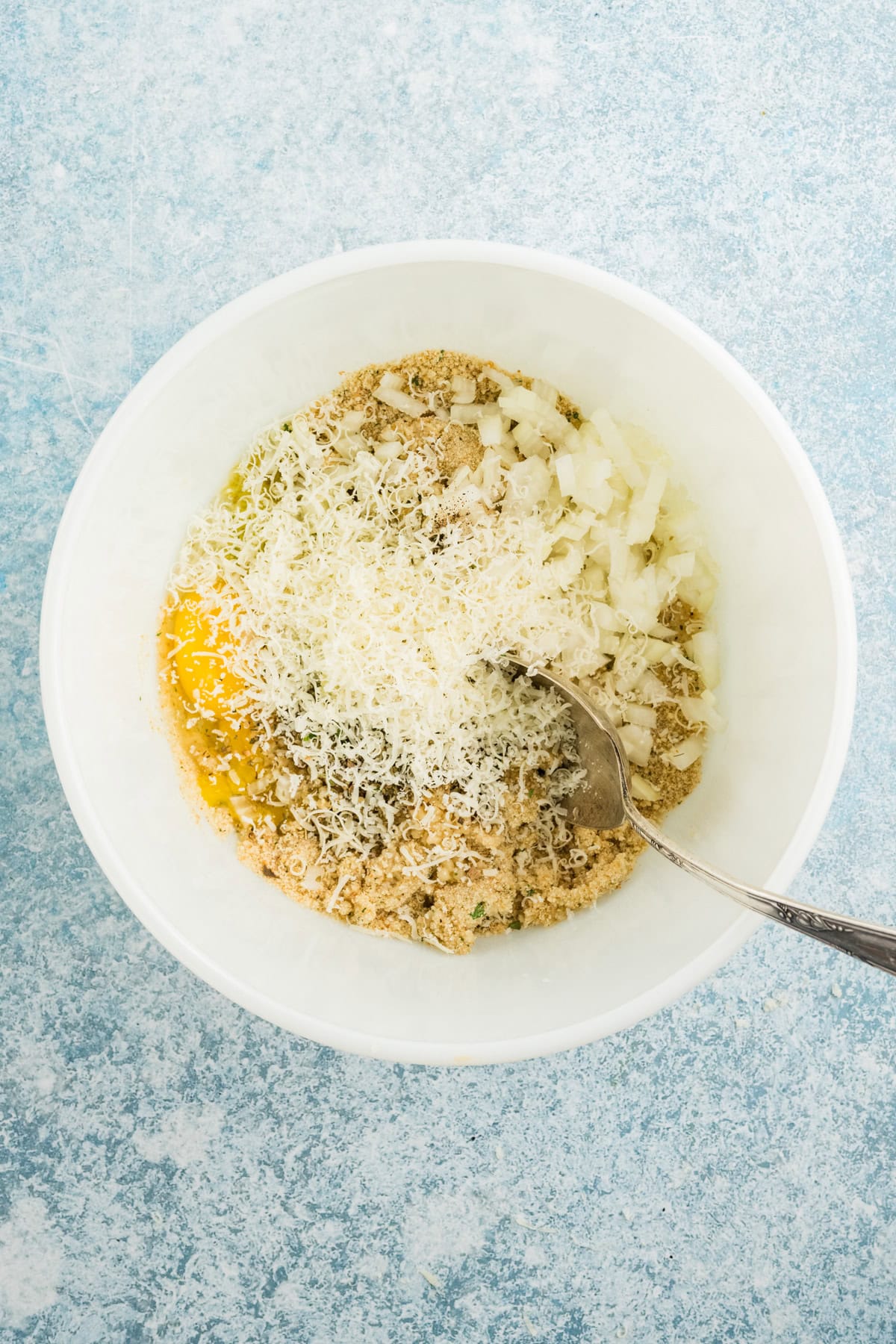 Aromatics, herbs, and parmesan cheese added to a bowl with egg and milk-soaked breadcrumbs.