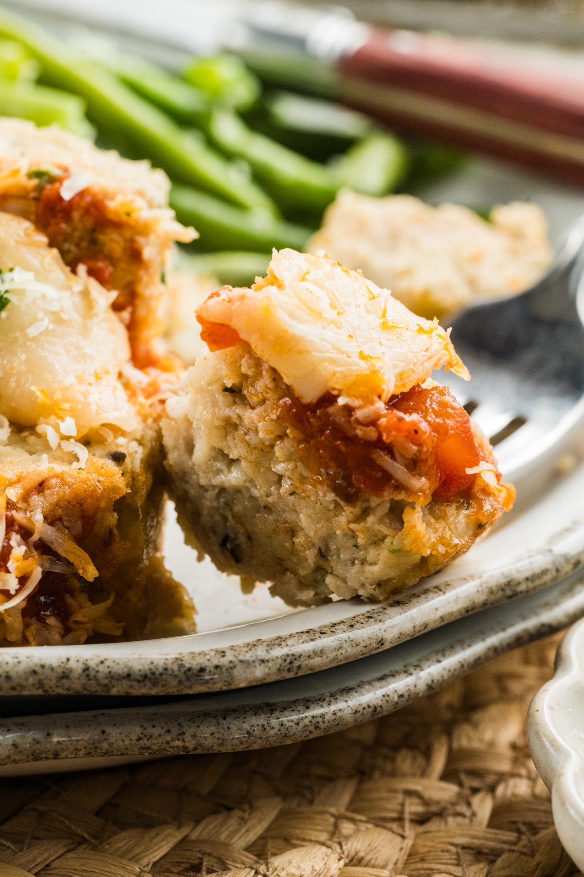 Fork holding a bite of parmesan chicken meatloaf at the edge of a plate.