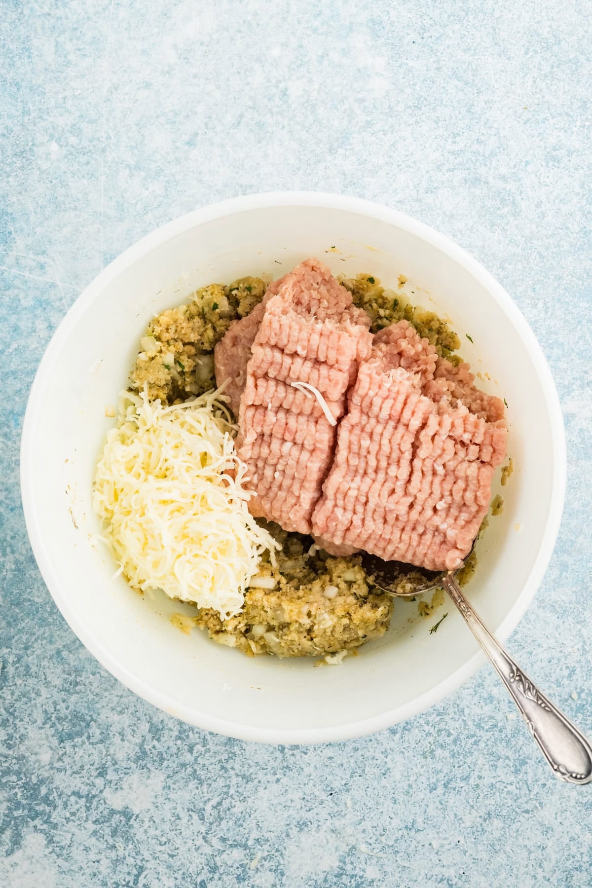 Adding ground chicken and mozzarella cheese to a mixing bowl for parmesan chicken meatloaf.