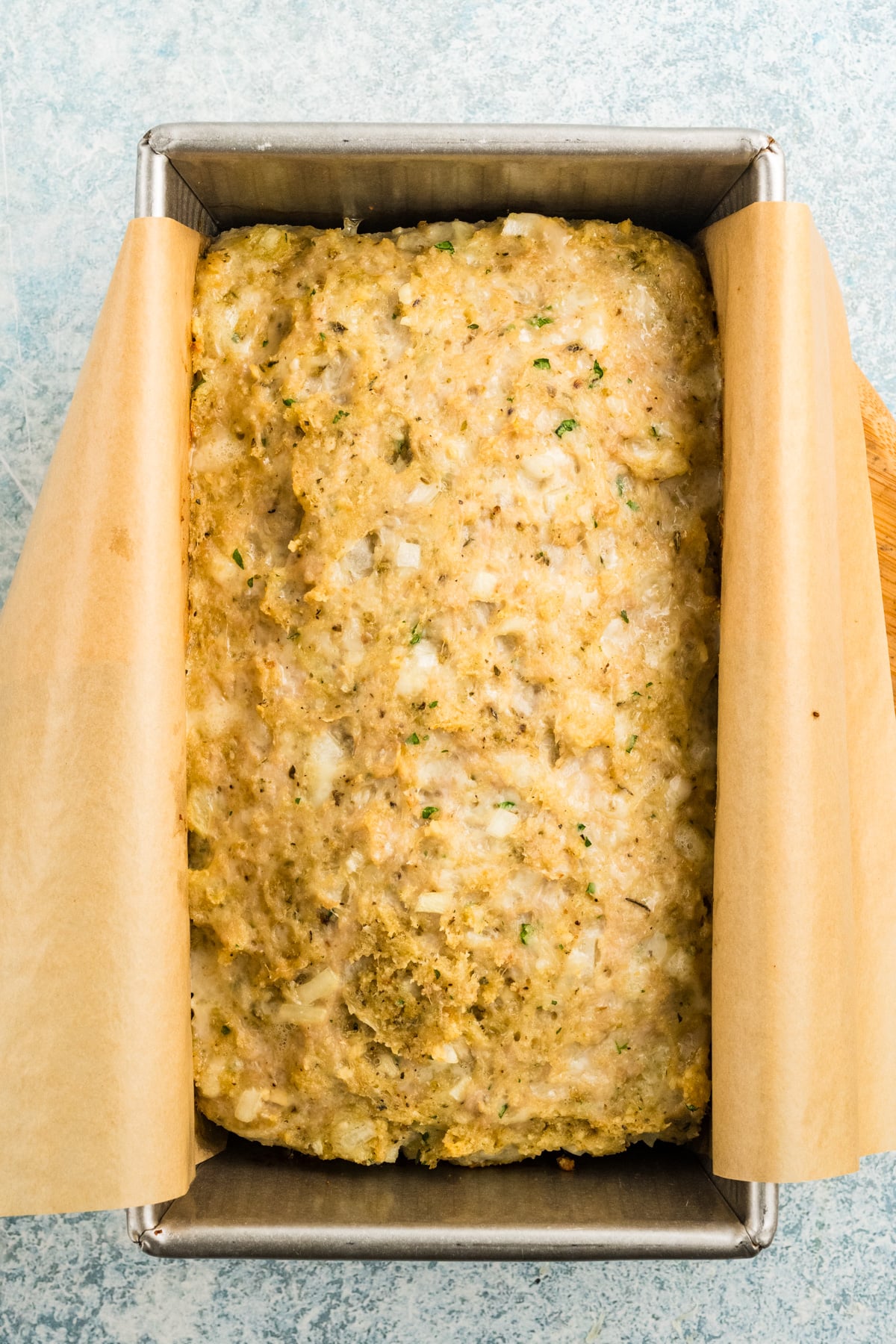Partly baked parmesan chicken meatloaf in a loaf pan.
