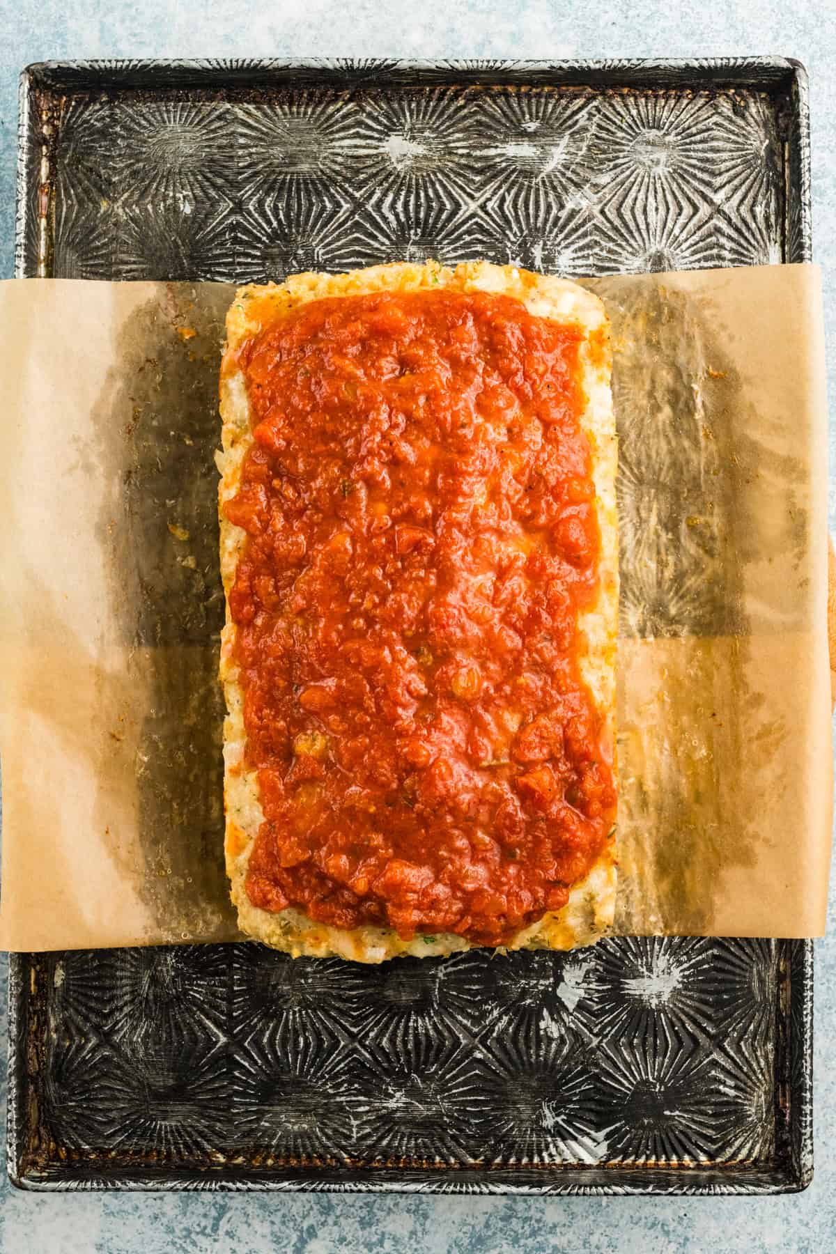 Parmesan chicken meatloaf removed from the pan and topped with marinara sauce.